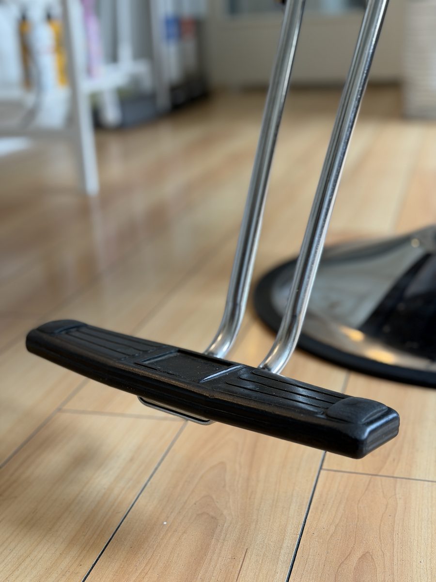 Close-up of a salon chair's footrest above a wooden floor
