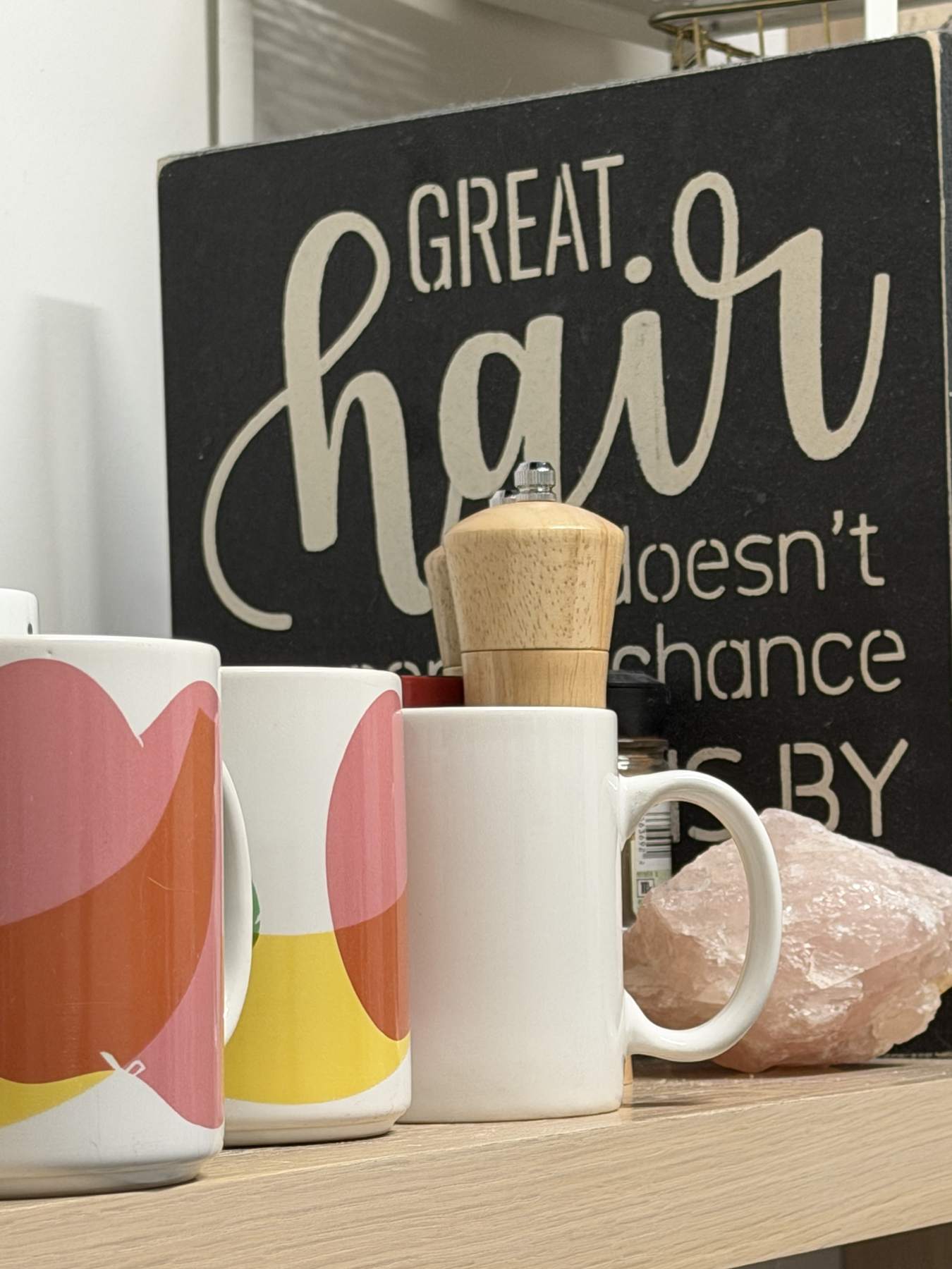 Coffee mugs in front of a sign that reads “Great hair doesn’t happen by chance”