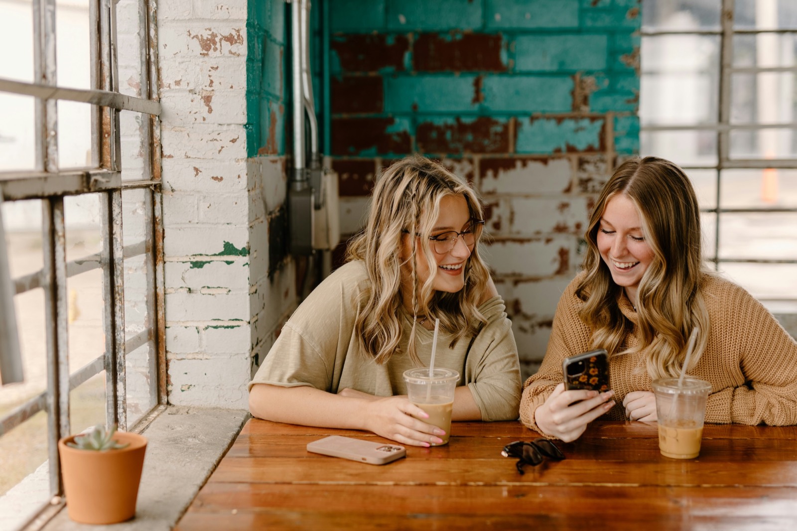 Two friends at a café table smiling at something on a phone