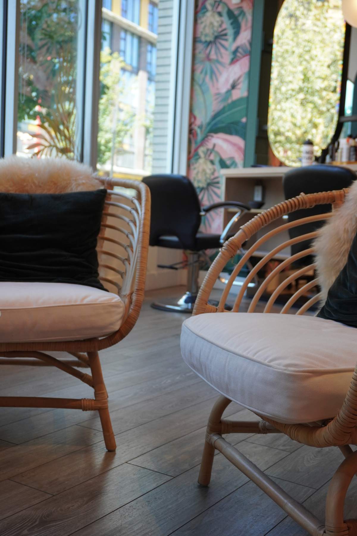 Rattan chairs in a salon waiting area beside tall windows