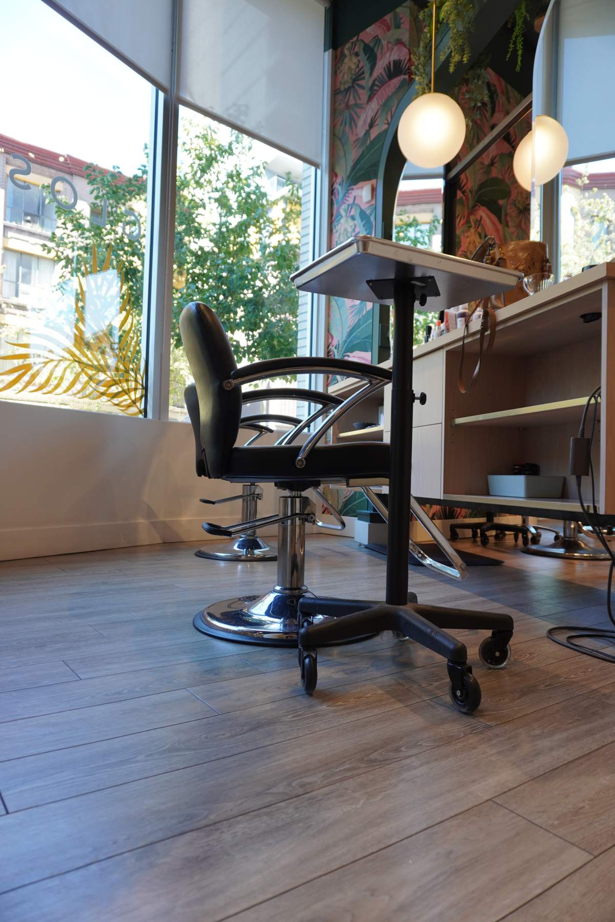 A black styling chair beside tall salon windows